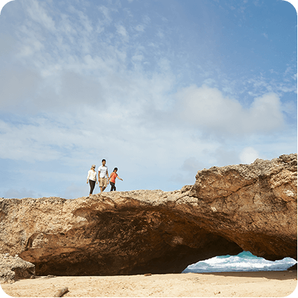 Three friends walking on top of natural stone bridge over waters of Aruba.