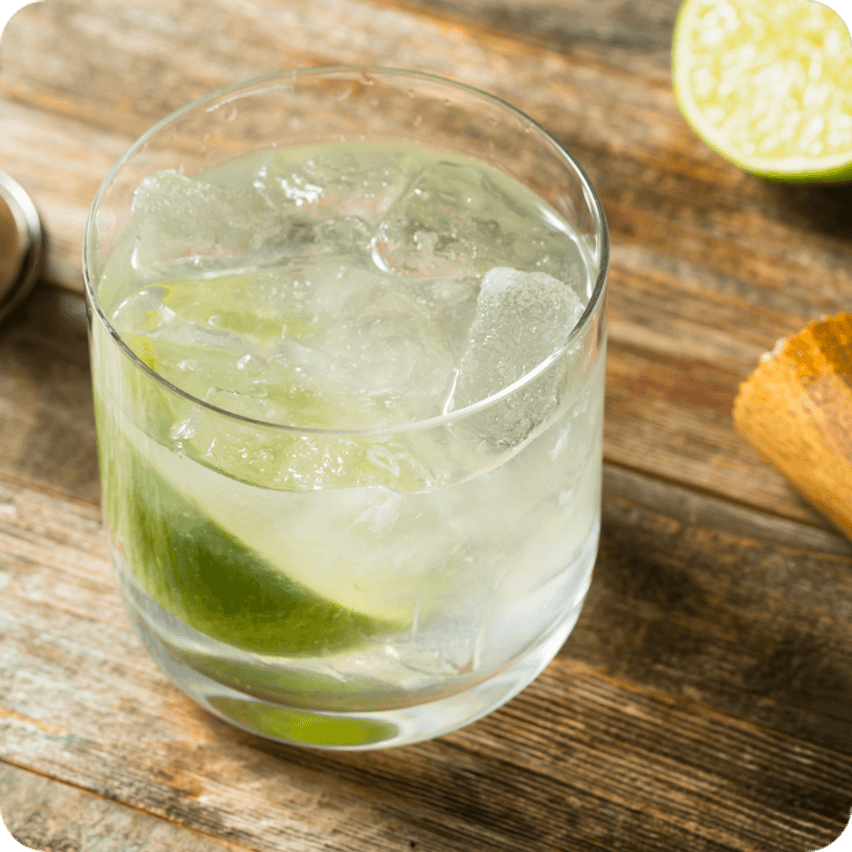 Drink with ice and lime on wooden tray.