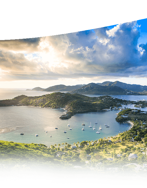 View from high point with open expanse of water and sailboats surrounded by green covered caribbean hills